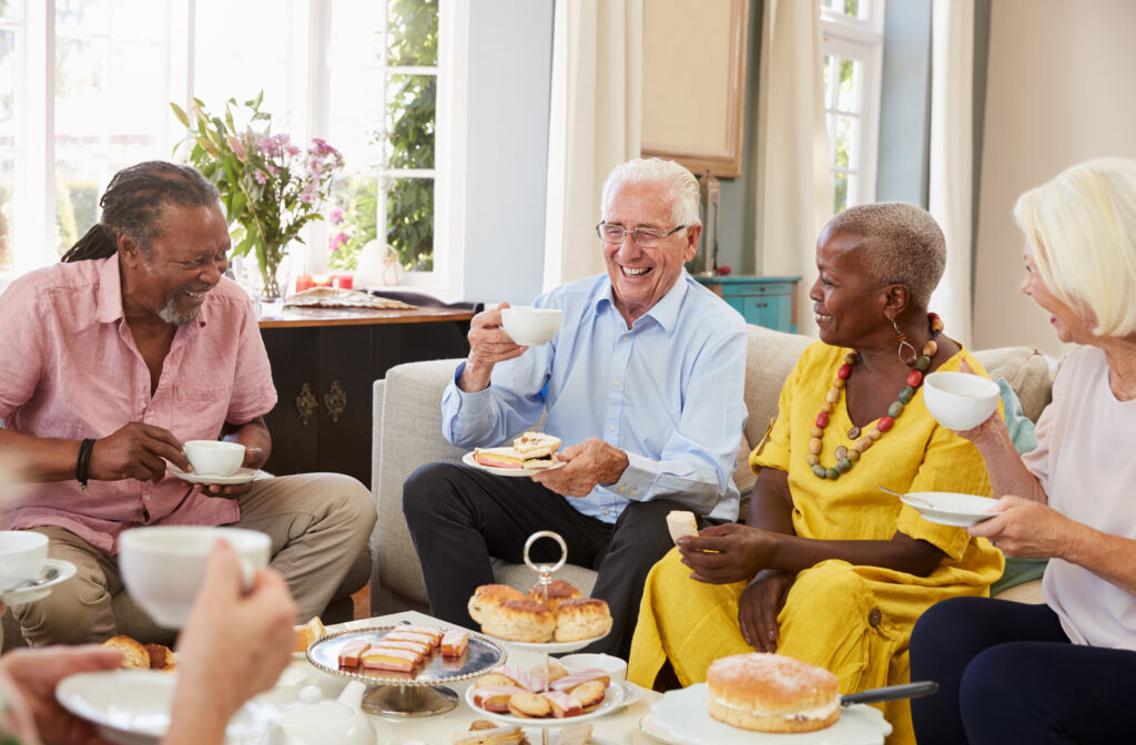 Senior couples socializing with one another in senior community living room while drinking tea and having snacks