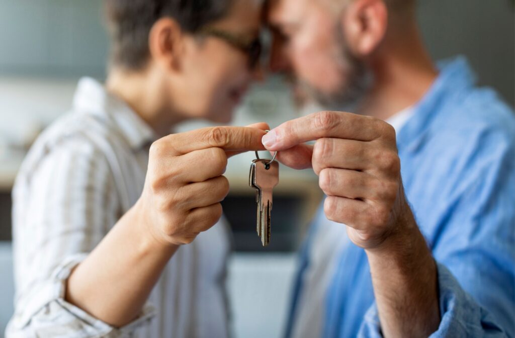 A senior couple rest their foreheads against each other while holding up the keys to their new living space up to the camera