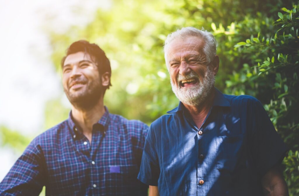 Two adults, one older and one younger, laughing together outdoors enjoying a sunny day