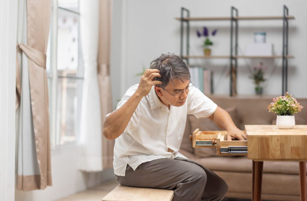 Senior man scratching his head as he digs through a desk drawer.