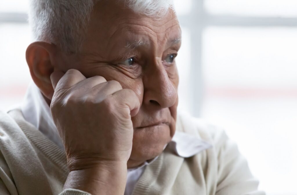A senior man brooding over something with his chin resting on his right hand, with his eyes looking afar.