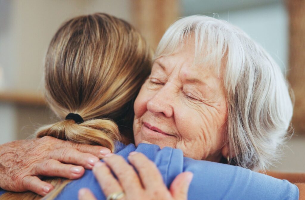 A close-up image of an older adult in assisted living smiling and hugging a caregiver.