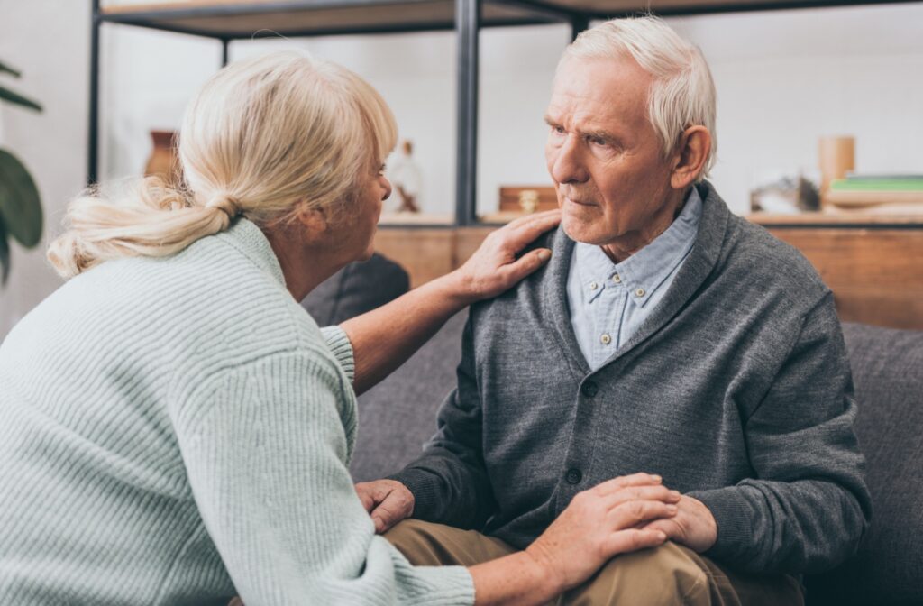 An older adult comforts their stressed spouse with mixed dementia on their couch at home